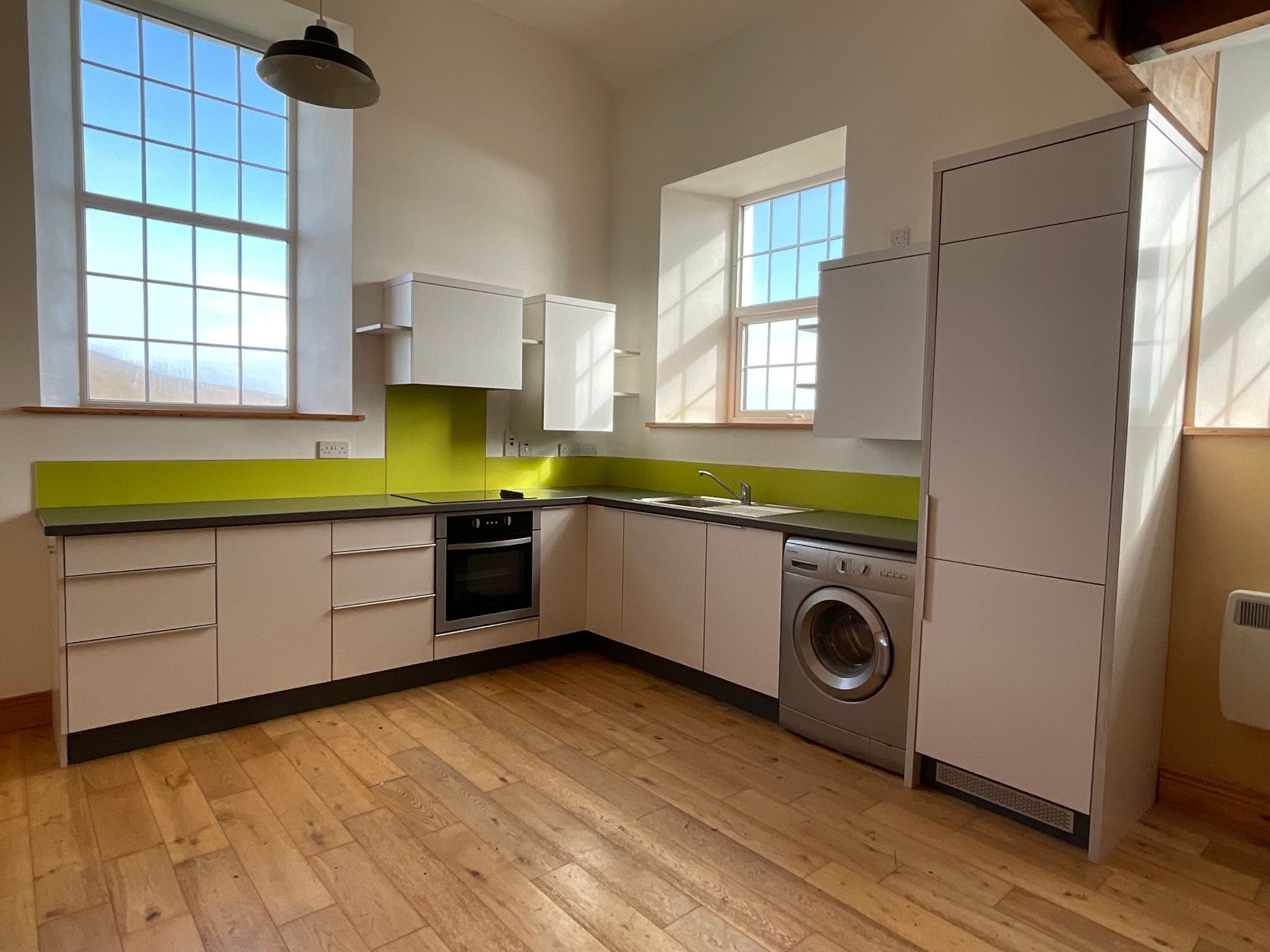 Kitchen with a green glass splashback and a tall larder